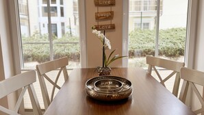 Een eettafel met een decoratieve schaal en een bloevas, met op de achtergrond een stadsgezicht door grote ramen.