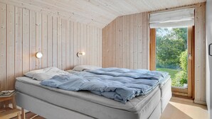 A bedroom with a bed, two wall-mounted lights, a wooden ceiling, and a large window with a view of greenery. - Stunning home in Væggerløse with sauna (Væggerløse)