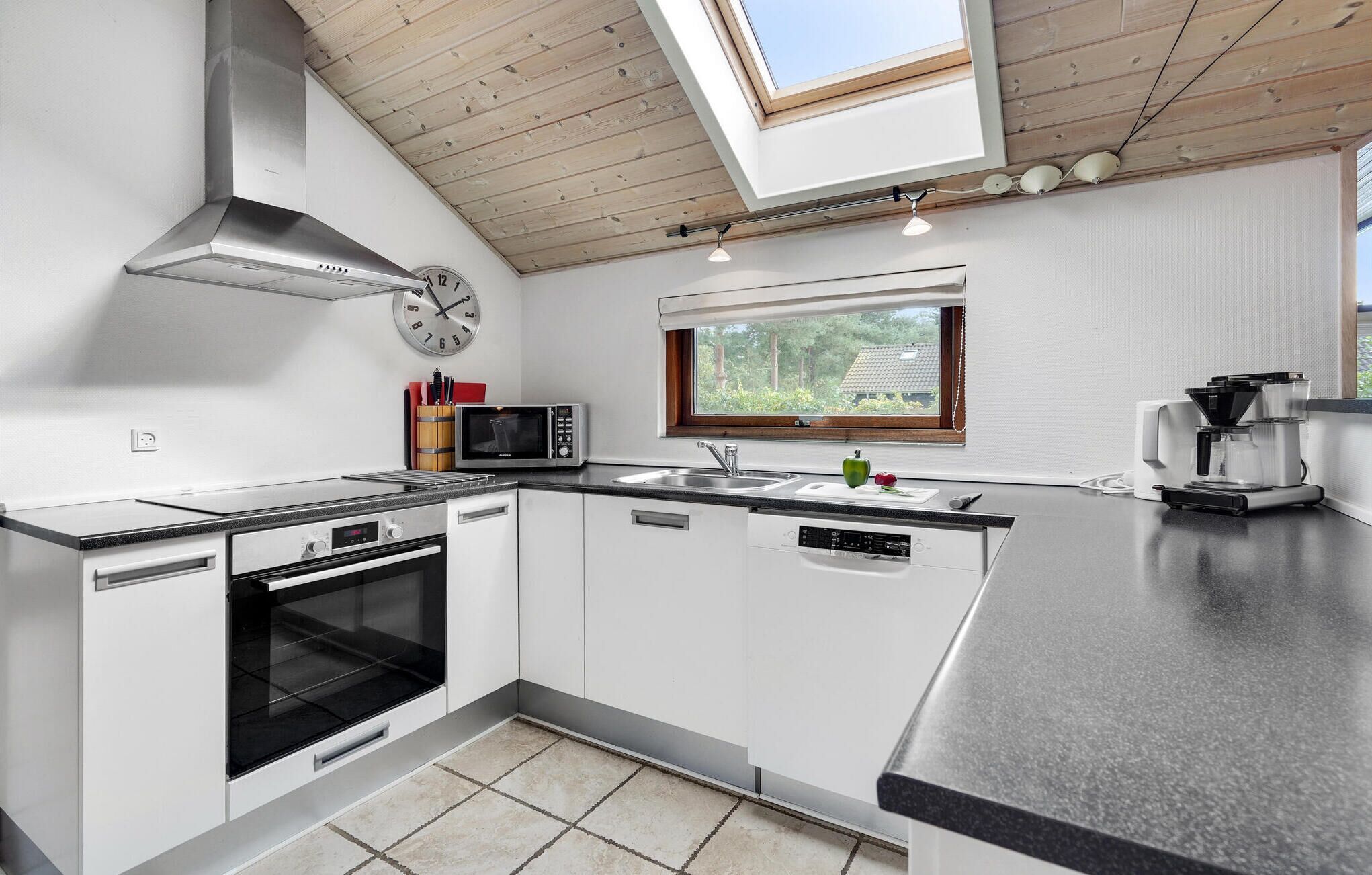 A modern kitchen with white cabinetry, a built-in oven, a microwave, a sink, and a coffee maker.