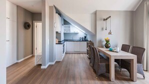 Une cuisine moderne avec des meubles blancs, un plan de travail noir et une table à manger en bois, accompagnée de chaises.