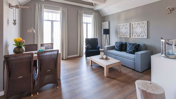 Un salon spacieux comprenant un coin repas, un canapé gris et un fauteuil bleu.