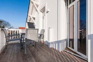 A wooden deck with a table and chairs, white walls, and a sliding glass door.