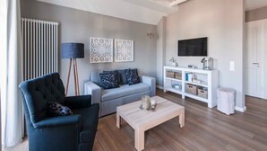 Un salon moderne avec un canapé gris, un fauteuil noir, une table basse en bois et un meuble de télévision blanc doté d’un écran plat.