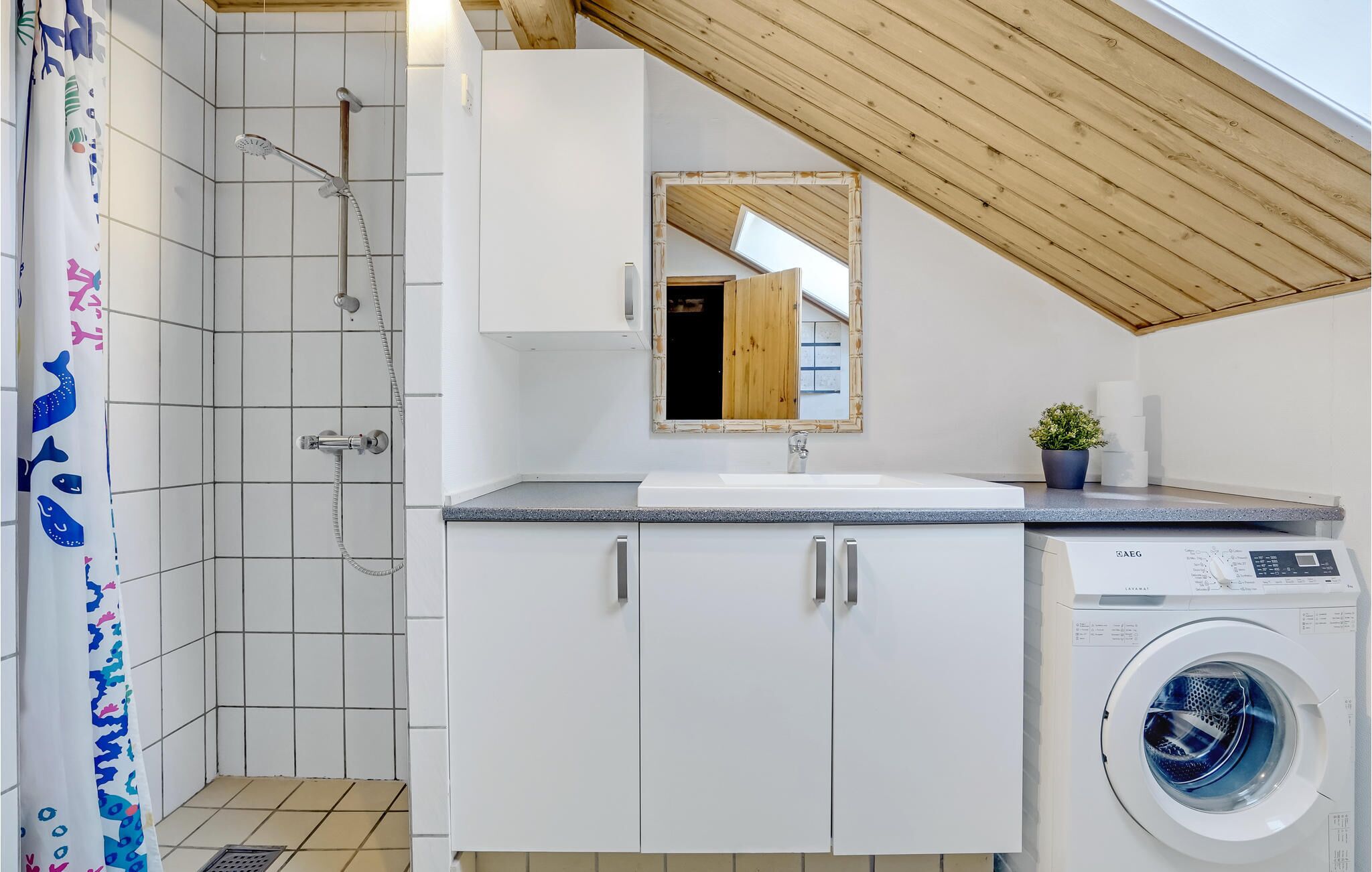 A modern bathroom with a shower, a sink, a mirror, and a washing machine.