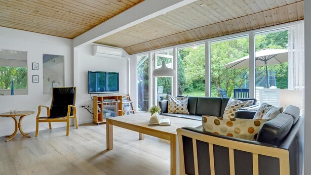 A spacious living room with a wooden ceiling, large windows, a TV, a sofa, and a dining table. - Lovely home in Oksbøl with sauna (Oksbøl)