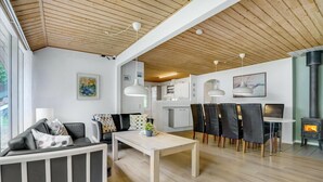 A modern living room with a sofa, dining table, and chairs, a kitchen area, and a fireplace. - Lovely home in Oksbøl with sauna (Oksbøl)