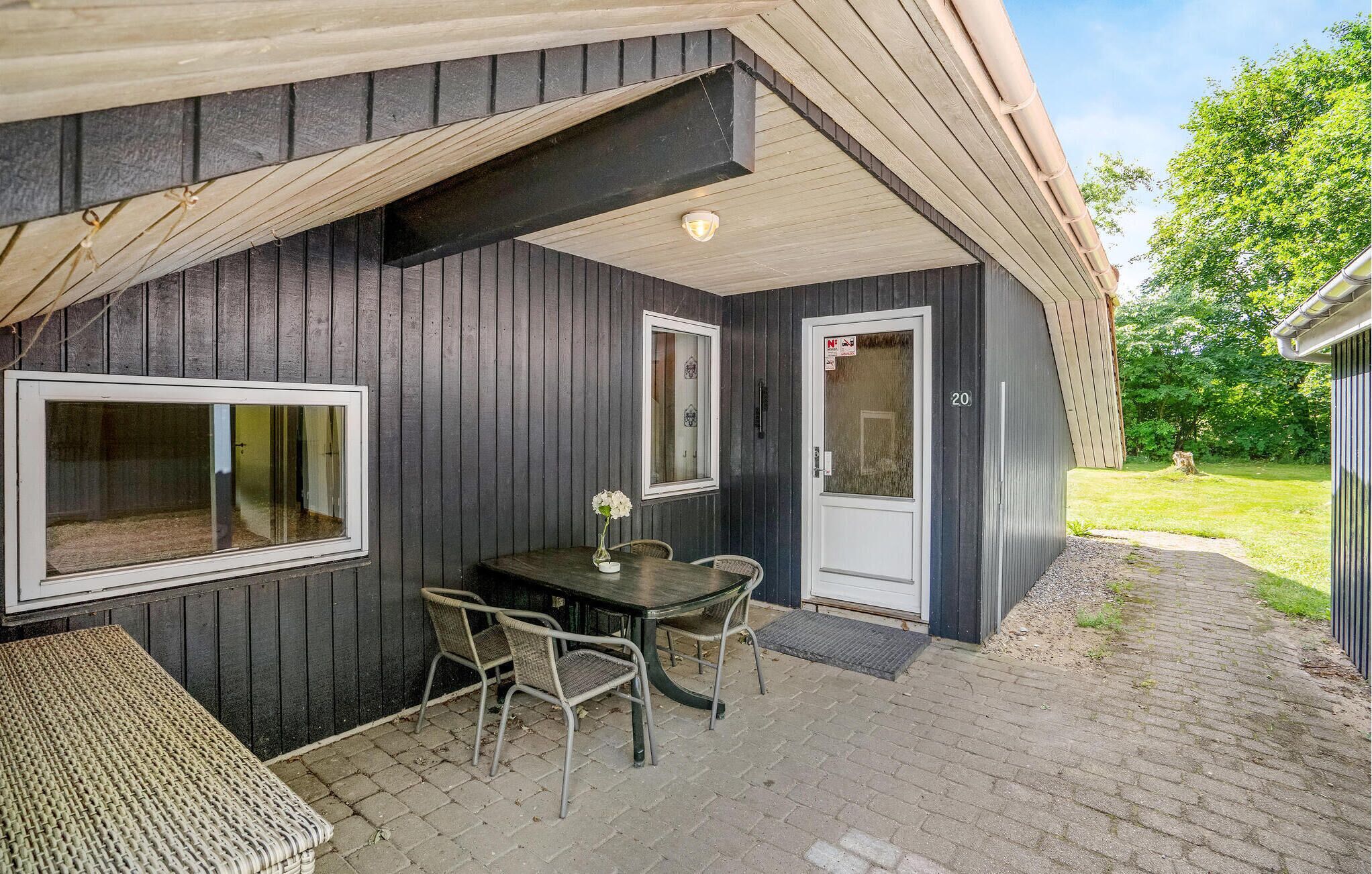 A covered outdoor seating area with a table and chairs, a door, and a window.