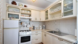 Una cocina con gabinetes blancos, estufa, refrigerador y pileta.