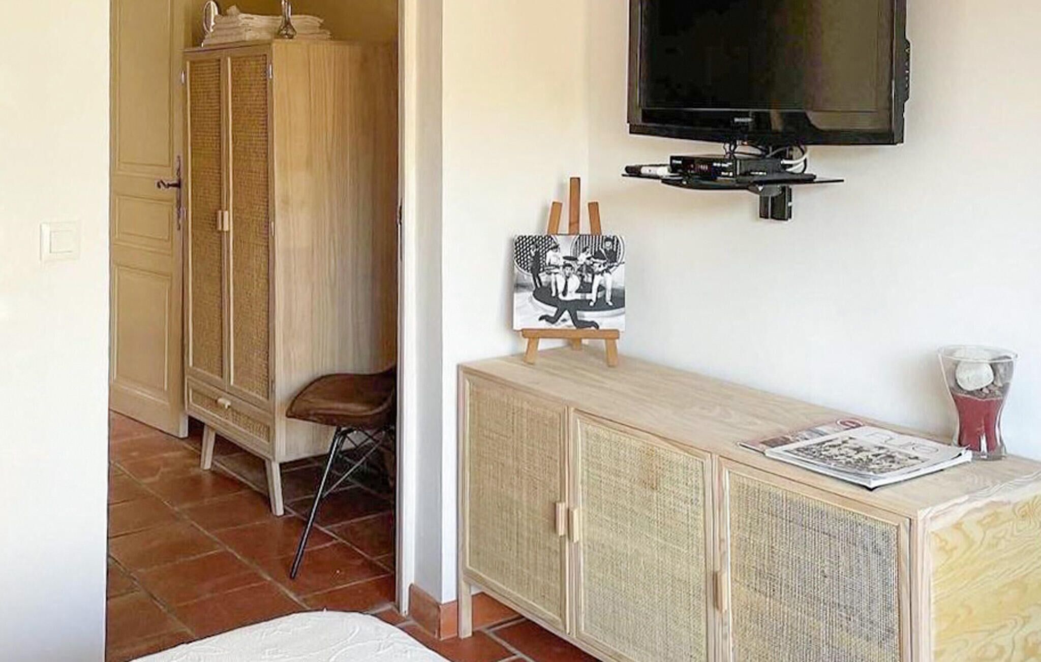 A room with a wooden cabinet, a television mounted on the wall, a small table with a newspaper, and a chair.