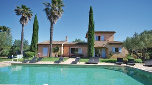 Un espace aménagé au bord de la piscine, avec des chaises longues, une piscine et un bâtiment à deux étages surmonté d’un toit en tuiles.