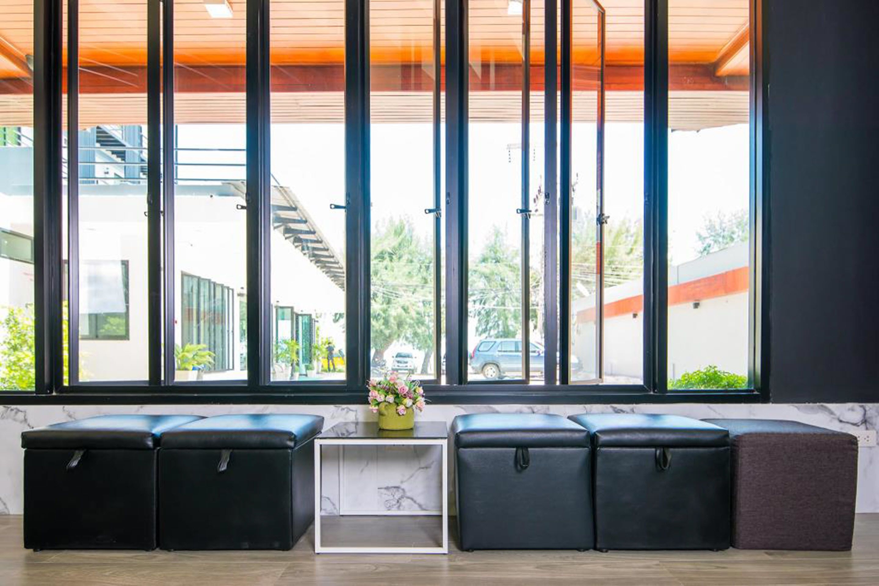 A modern interior with a seating area by large windows, a marble accent wall, and a small white shelf with flowers.