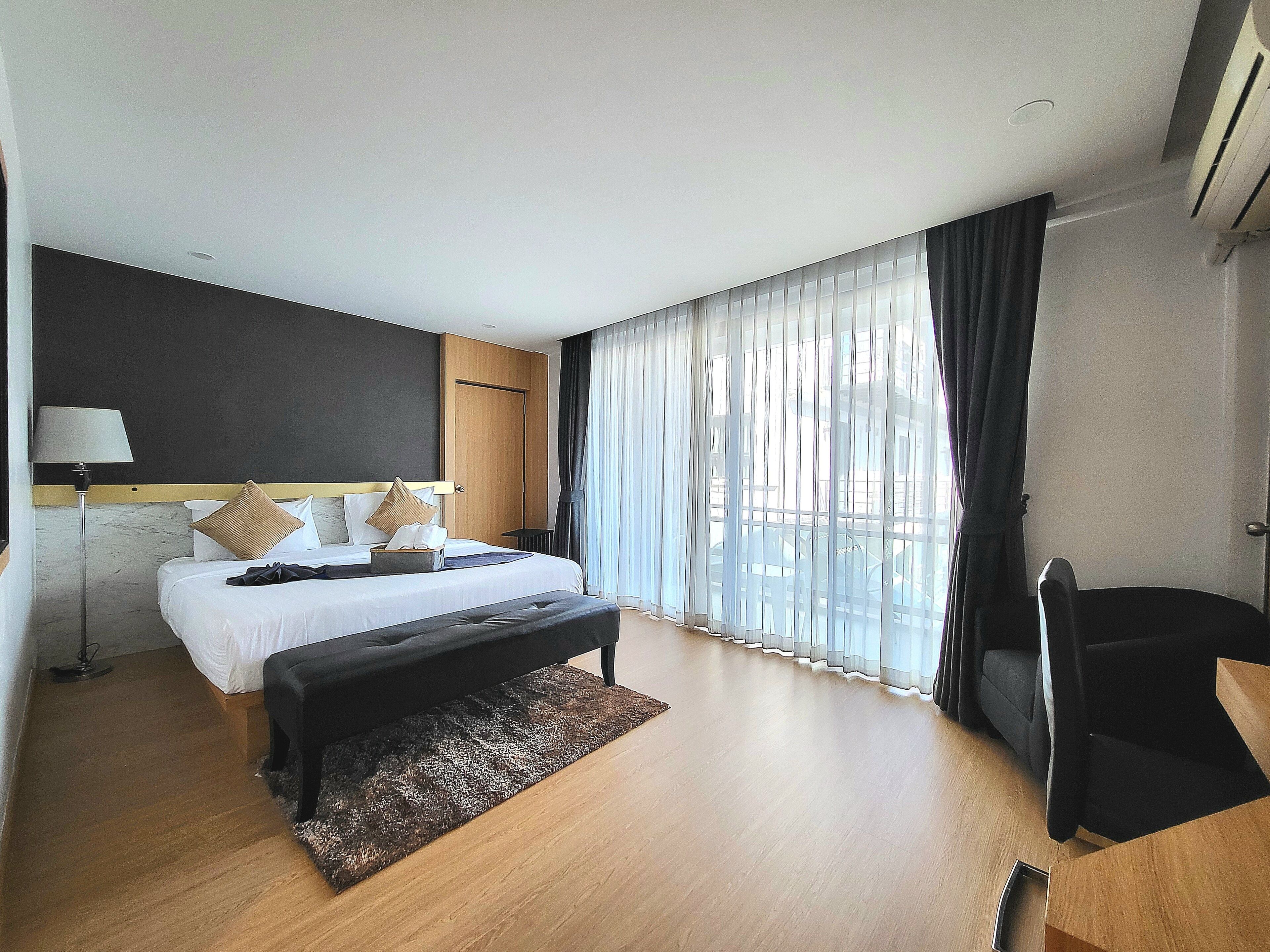 Una habitación de hotel moderna con una cama grande, un escritorio y vistas a la ciudad a través de cortinas translúcidas.