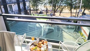 A balcony with a table set for breakfast, overlooking a street with parked cars and trees. - Irin Beach Cha - am (Cha-am)