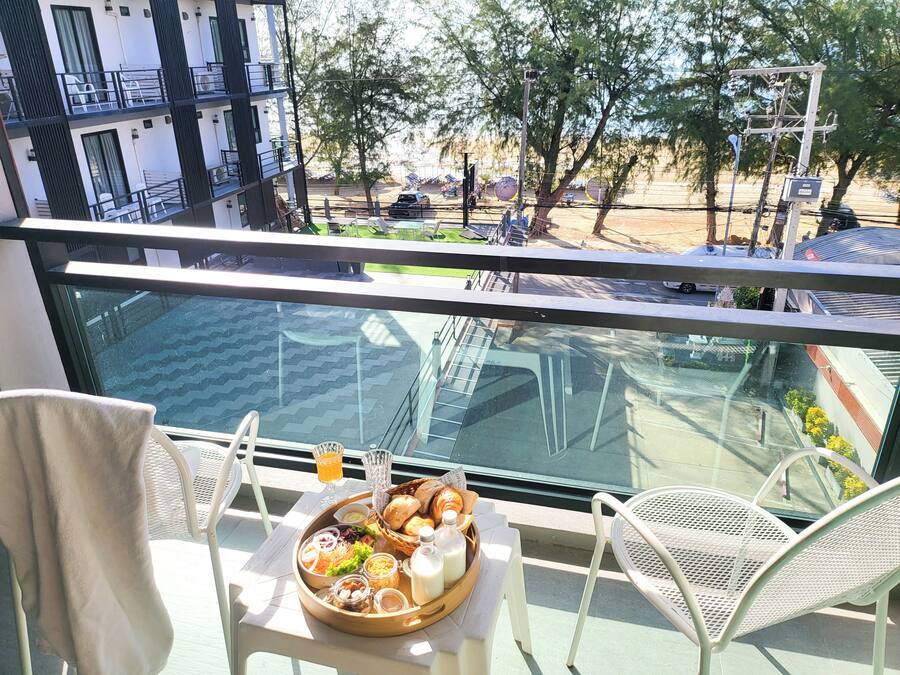 Un balcón con una mesa dispuesta para el desayuno, con vistas a una calle con coches aparcados y árboles.
