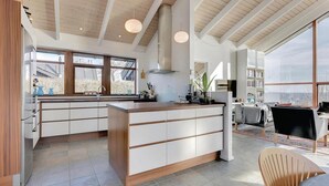 A modern kitchen with a central island, large windows, and a dining area with a view.