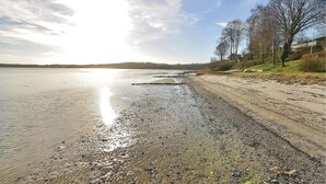 A beach with pebbles and sand, a clear sky, and trees in the background.
