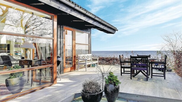 A modern house with large glass windows, a wooden deck, and outdoor furniture.