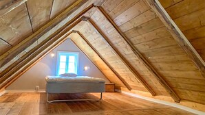 Une petite chambre mansardée avec un lit simple, une fenêtre et des poutres en bois.