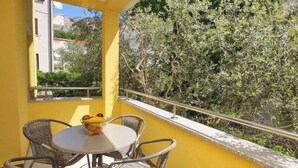 Un balcón con sillas de mimbre y una mesa, una pared amarilla y vistas a árboles y edificios.