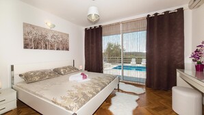 Une chambre avec un lit, un tableau, une fenêtre avec des rideaux, une vue sur la piscine et un tapis blanc et moelleux.