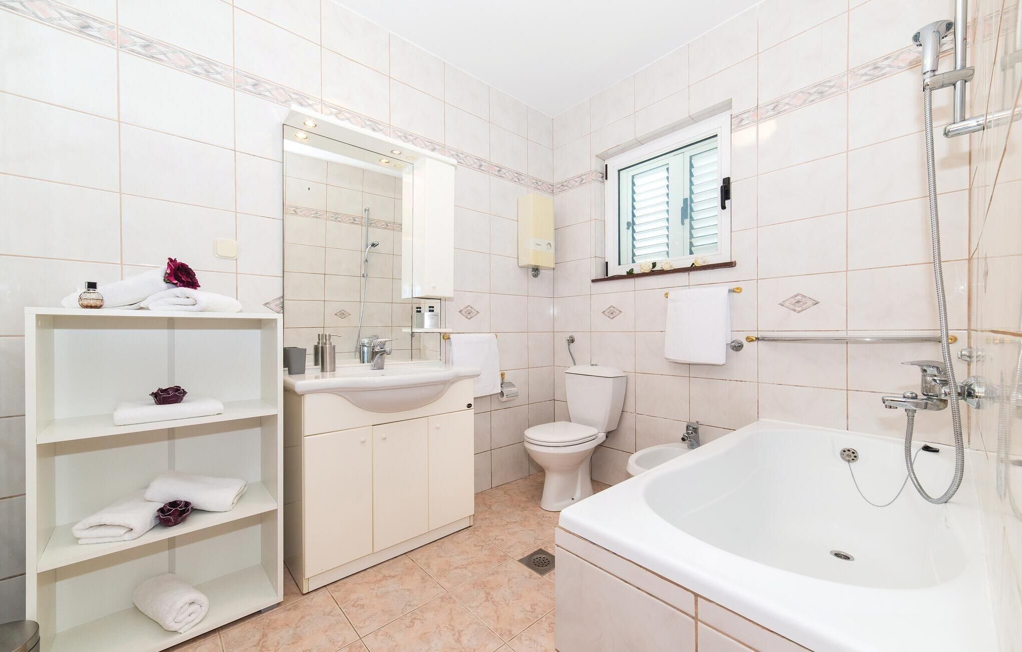 A modern bathroom with a large bathtub, a sink, a toilet, and a vanity with shelves holding towels and toiletries.