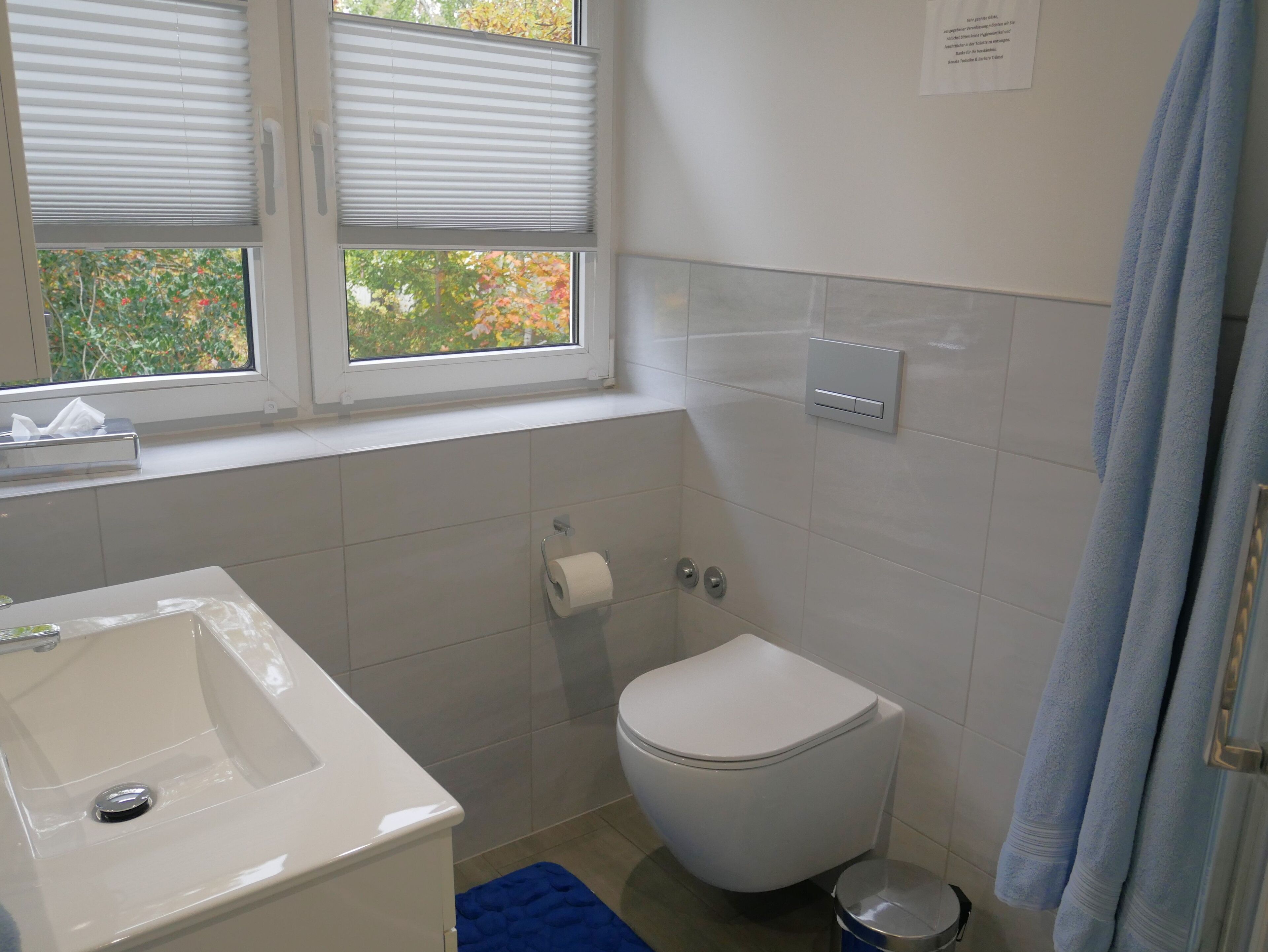Et badeværelse med hvid vask, toilet og et vindue med persienner.