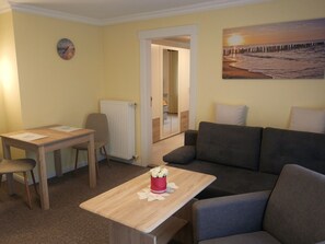 A room with a wooden table, a gray sofa, a radiator, and a painting of a beach scene.