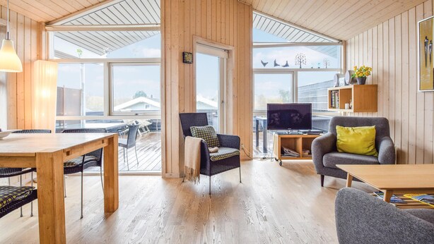 Amplia sala de estar con techo alto, ventanas grandes y comedor con mobiliario de madera.