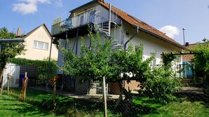 A two-story house with a balcony, a fenced yard, and a clear sky. - Vacation apartment with garden terrace - Holiday apartments with terrace (Patzig)