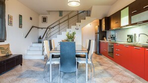 Eine moderne Küche mit roten Schränken, ein Essbereich mit Tisch und Stühlen sowie eine Treppe mit Geländer.