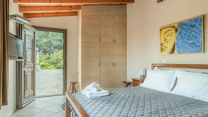 Ein Schlafzimmer mit Bett, Kleiderschrank, einem Gemälde und Blick ins Grüne.