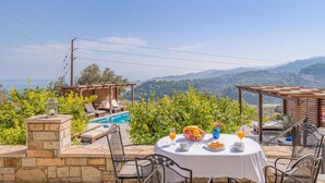 Eine Terrasse mit Pool, Sitzgelegenheiten im Freien und einem Frühstückstisch mit Obst und Getränken.