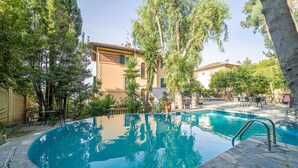 A swimming pool surrounded by stone tiles, with lounge chairs and tables, and buildings in the background. - Lovely apartment in Rapallo GE with WiFi (Rapallo GE)