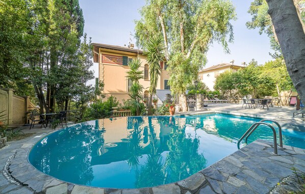 A swimming pool surrounded by stone tiles, with lounge chairs and tables, and buildings in the background. - Lovely apartment in Rapallo GE with WiFi (Rapallo GE)
