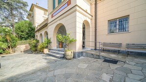 A stone-paved courtyard with a bench, a large potted plant, and a building with arched windows and a balcony. - Lovely apartment in Rapallo GE with WiFi (Rapallo GE)