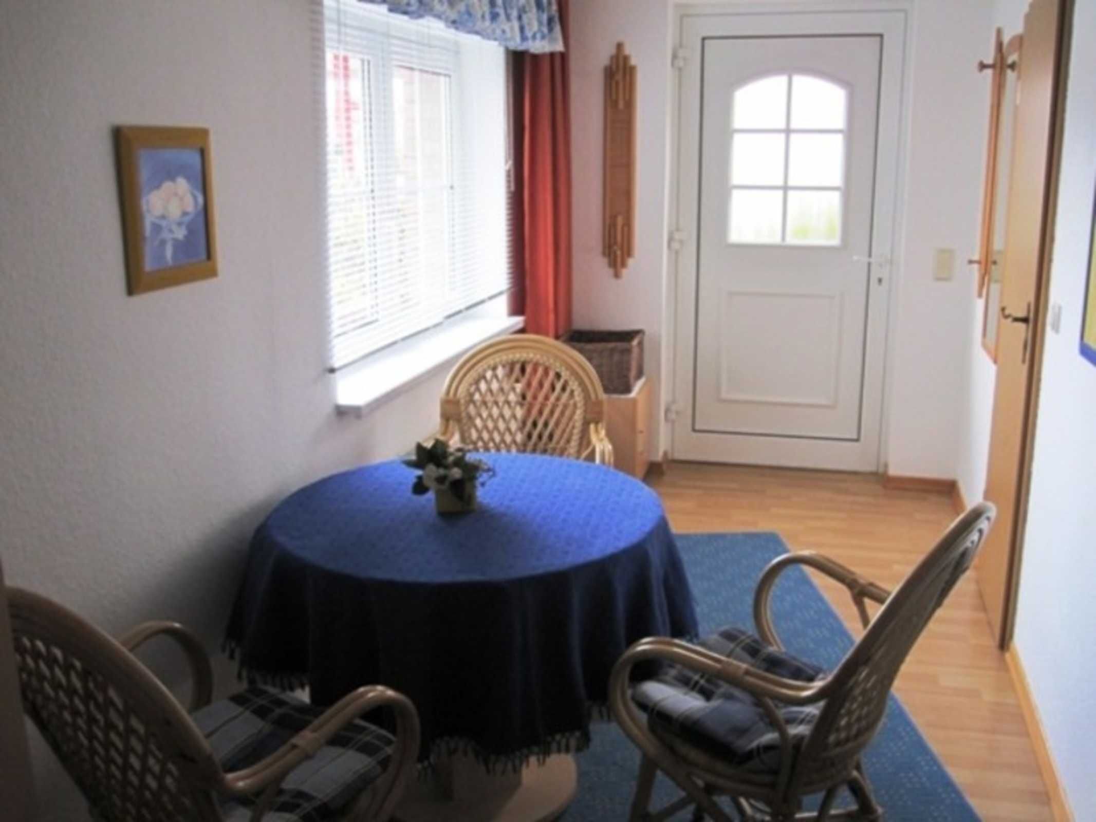 Een eetgedeelte met een ronde tafel, bedekt met een blauwe tafelkleed, omringd door rieten stoelen.