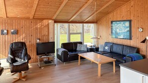 A wooden-paneled room with a sofa, a chair, a TV on a stand, and a painting on the wall. - Nice home in Sydals with sauna (Sydals)