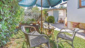 Un patio con sedie in vimini, un tavolo e una bottiglia di vino sotto un ombrello blu.