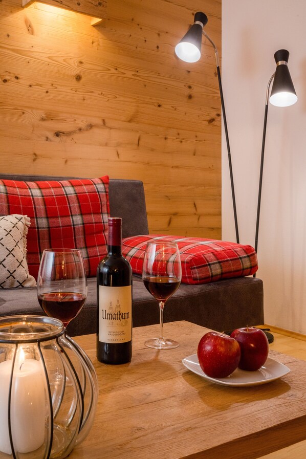 A cozy room with a wooden wall, a plaid sofa, a table with a wine bottle, glasses, and apples.