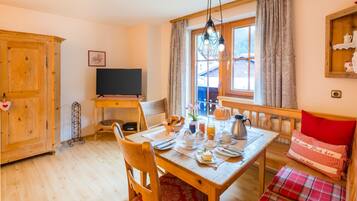 A dining area with a wooden table set for breakfast, a television, and a window with curtains.