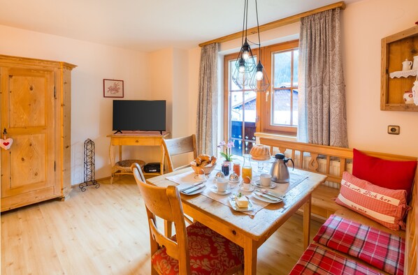 A dining area with a wooden table set for breakfast, a television, and a window with curtains.