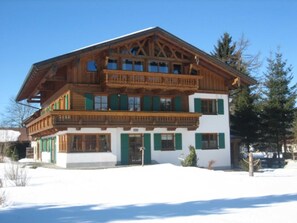 A multi-story wooden chalet with balconies, white walls, and green shutters.