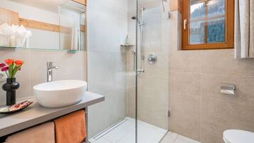 A modern bathroom with a glass-enclosed shower, a white sink, and a window with a view of trees.