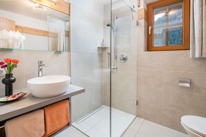 A modern bathroom with a glass-enclosed shower, a white sink, and a window with a view of trees.