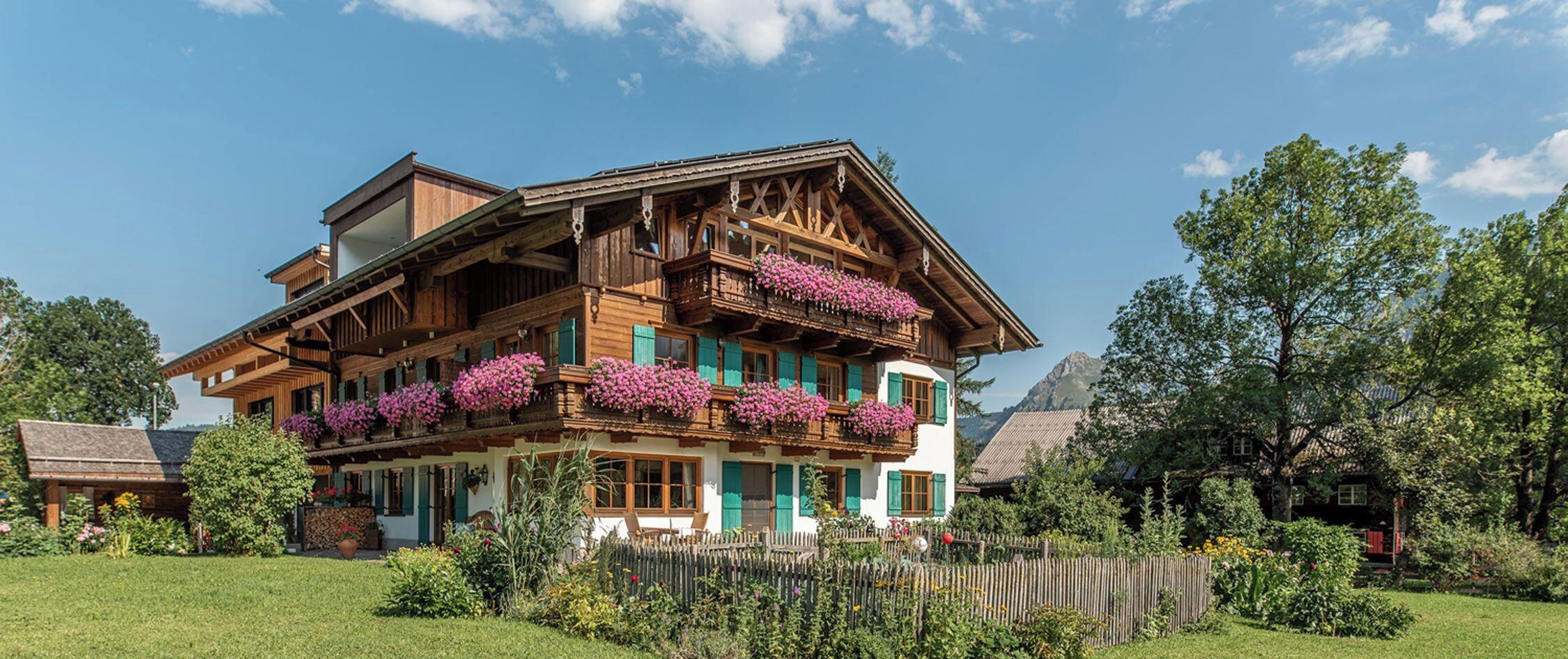 A traditional chalet with multiple balconies adorned with flowers, surrounded by a well-maintained garden.