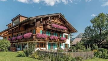 A traditional chalet with multiple balconies adorned with flowers, surrounded by a well-maintained garden.