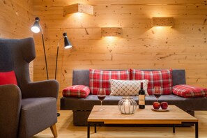 A cozy room with a sofa, armchair, and a table with wine and apples. - Suite Landleben - The bakery estate at Haldensee (Haldensee)