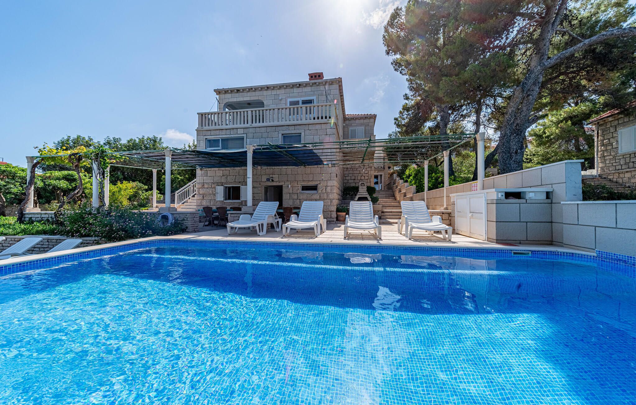 A swimming pool with lounge chairs, a stone building with a balcony, and a pergola.