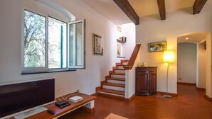 A living room with a TV, a wooden bench, a staircase, and a floor lamp. - Nice home in Le Grazie -SP- with WiFi (Le Grazie -SP-)