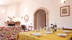 A dining area with a yellow tablecloth, white plates, wine glasses, and a fireplace.